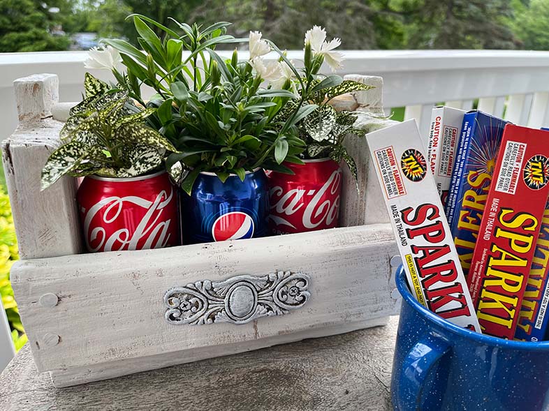 Coke and Pepsi soda cans turned planters and placed in a wood holder with sparklers in front.