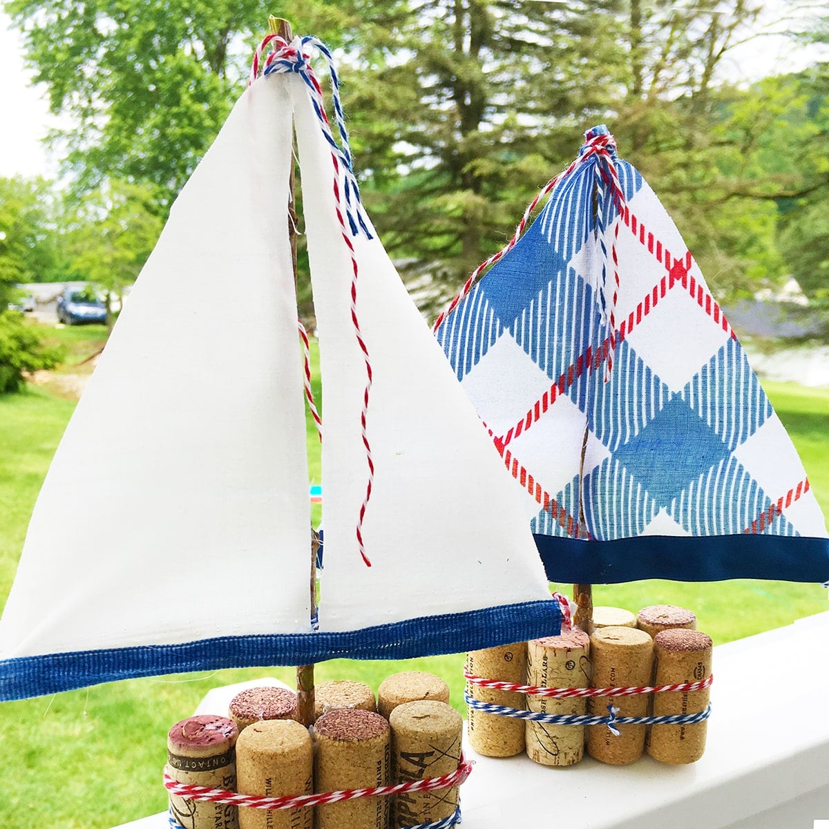 Square photo of two DIY Cork Sail Boats with greenery in the background.