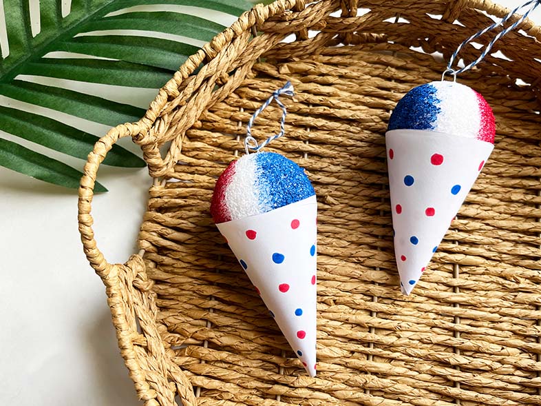 Feature image of finished DIY Snow Cone Ornaments on a wicker basket with a palm leaf in the background.