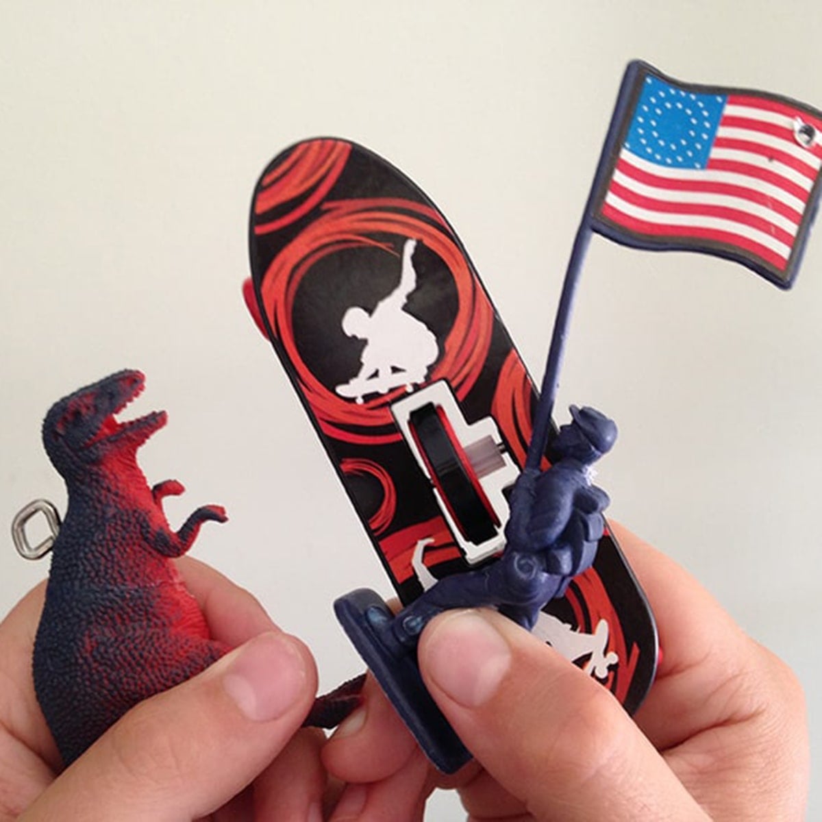 Square closeup of three small toys, dinosaur, army man with flag and skateboard used to make a kids room toy mobile.