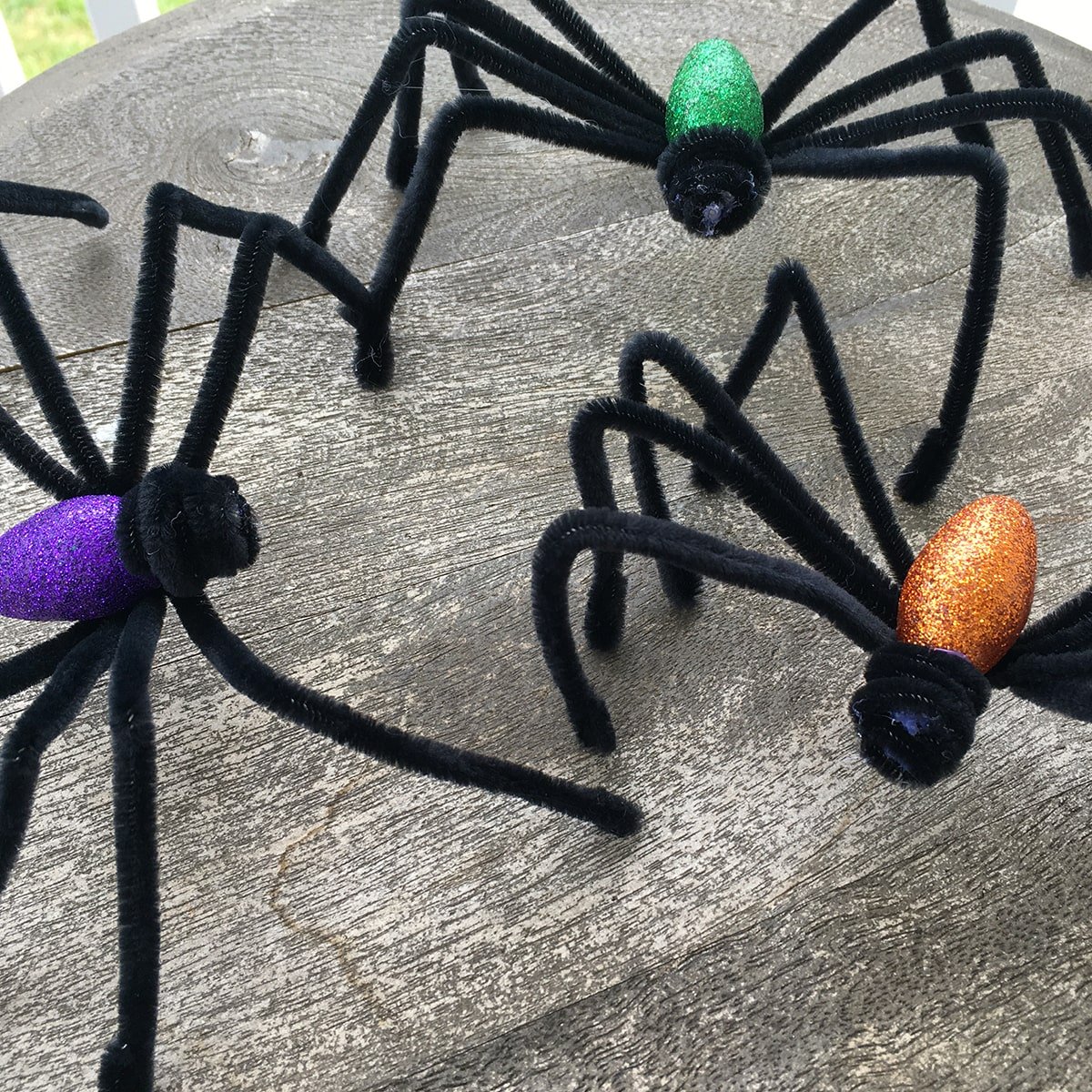 Closeup of three glitter spiders, purple, orange and green.