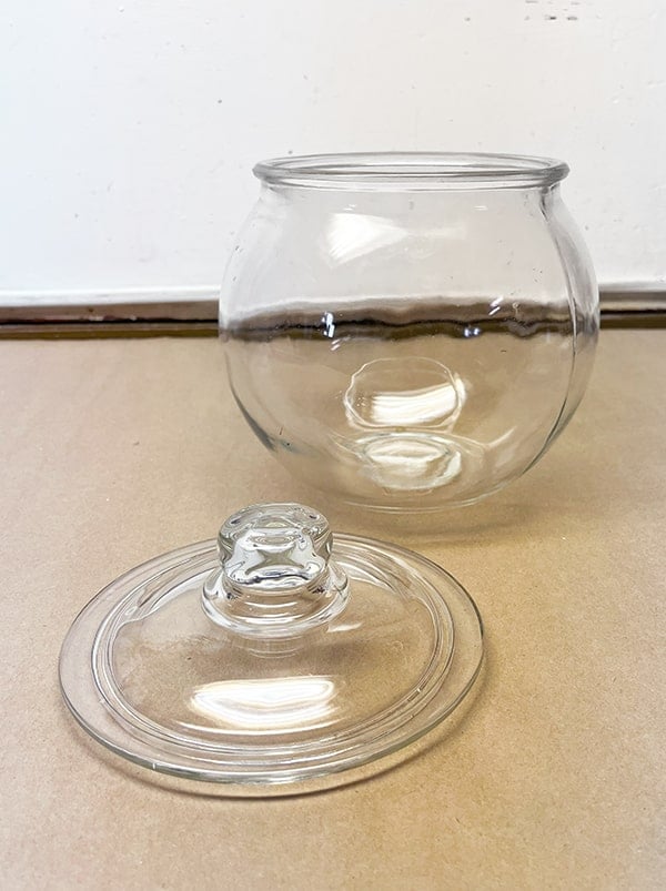 Before photo of a clear glass bowl. It is round with a lid to the side. This jar will be transformed into a mercury glass jack-o-lantern to add to a vintage Halloween decor display.