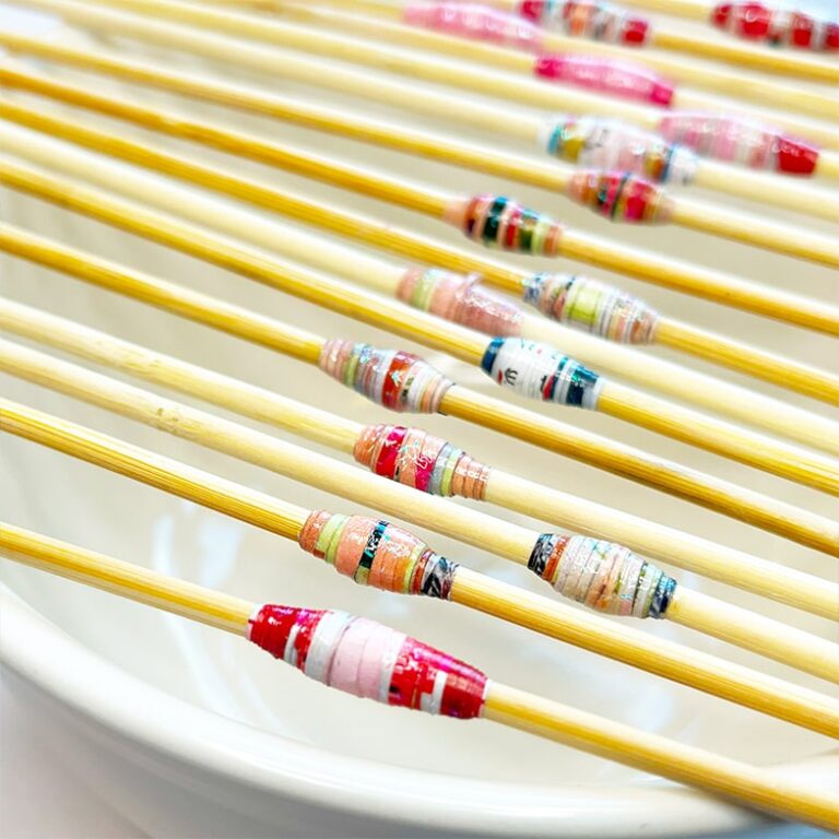 Photo of multiple colorful paper beads drying on a skewers.