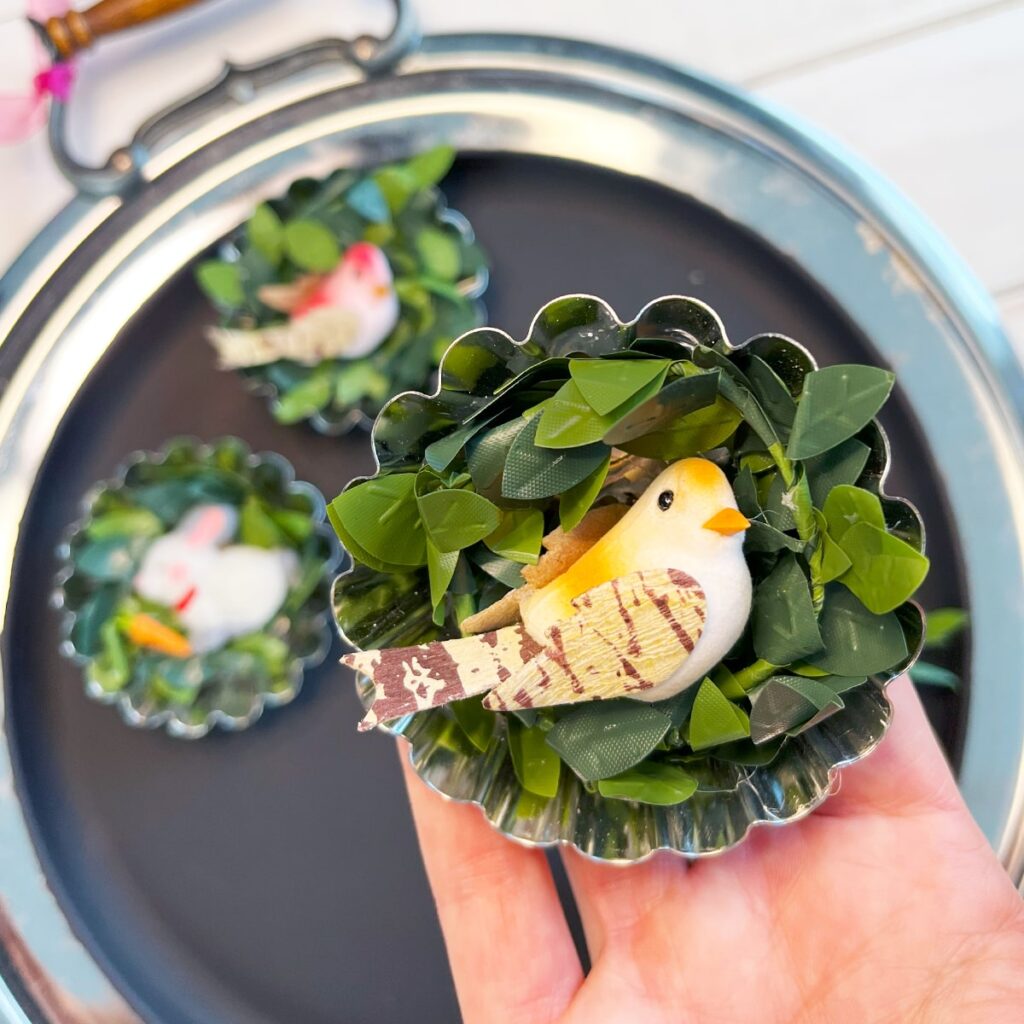 Closeup up photo holding a round fluted silver tart tin filled with a spiral of spring boxwood greenery and a small yellow bird placed in the center to finish this beautiful spring magnet.