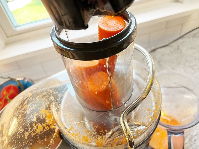 Closeup photo of feeding carrots into a wide mouth feed tube on a Breville Fountain Juicer. Two to three carrots can be juiced at a time in this juicer.