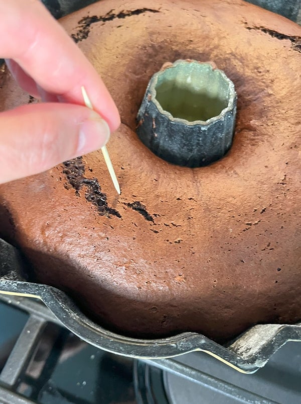 Closeup photo of a cake fresh from the oven being tested for doneness with a toothpick. If the toothpick comes out clean then the cake has baked evenly through.