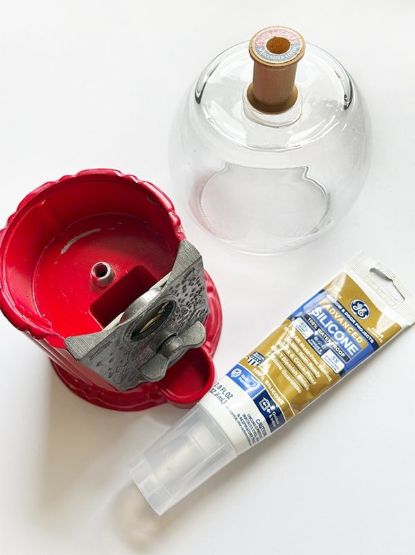Overhead view of silicone adhesive used to glue a wood spool to the bottom of a clear bubble vase that will sit on the red gumball machine base that has a center piece sticking up. It will act as a pin to keep the vase from moving.