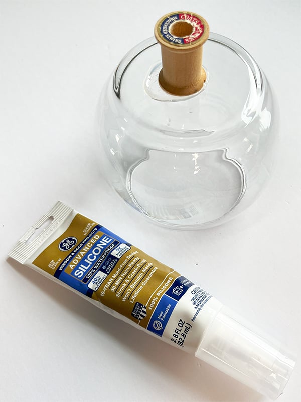 Glass globe vase from Dollar tree show in the process of adding a wood thread spool to act as a pin to keep the vase from sliding on the gumball machine base.