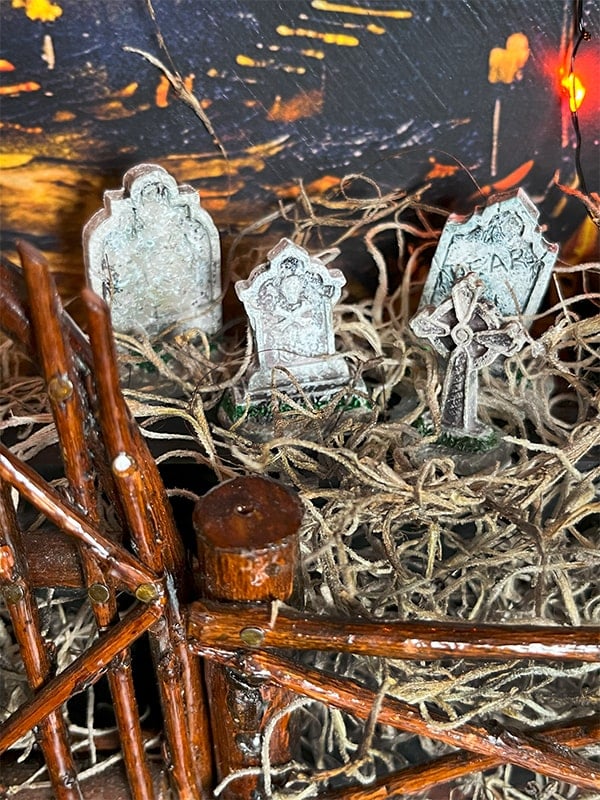 Closeup photo of a mini graveyard in a DIY Halloween miniature scene. There are four gravestones measuring about 3/4" each surrounded by Spanish moss.