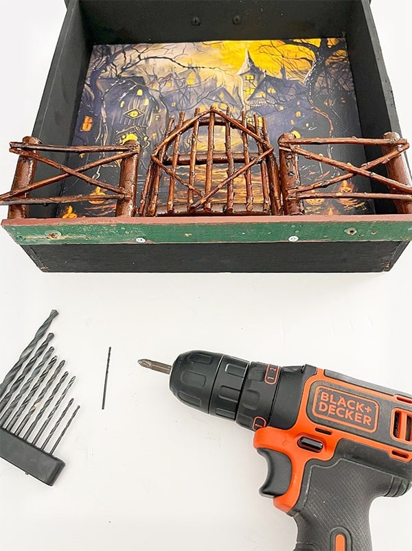 Photo of the bottom of my Halloween miniature scene. Shown is the bottom of the drawer where I used two wood screws and a drill in the foreground used to attach a mini fence for my graveyard scene.