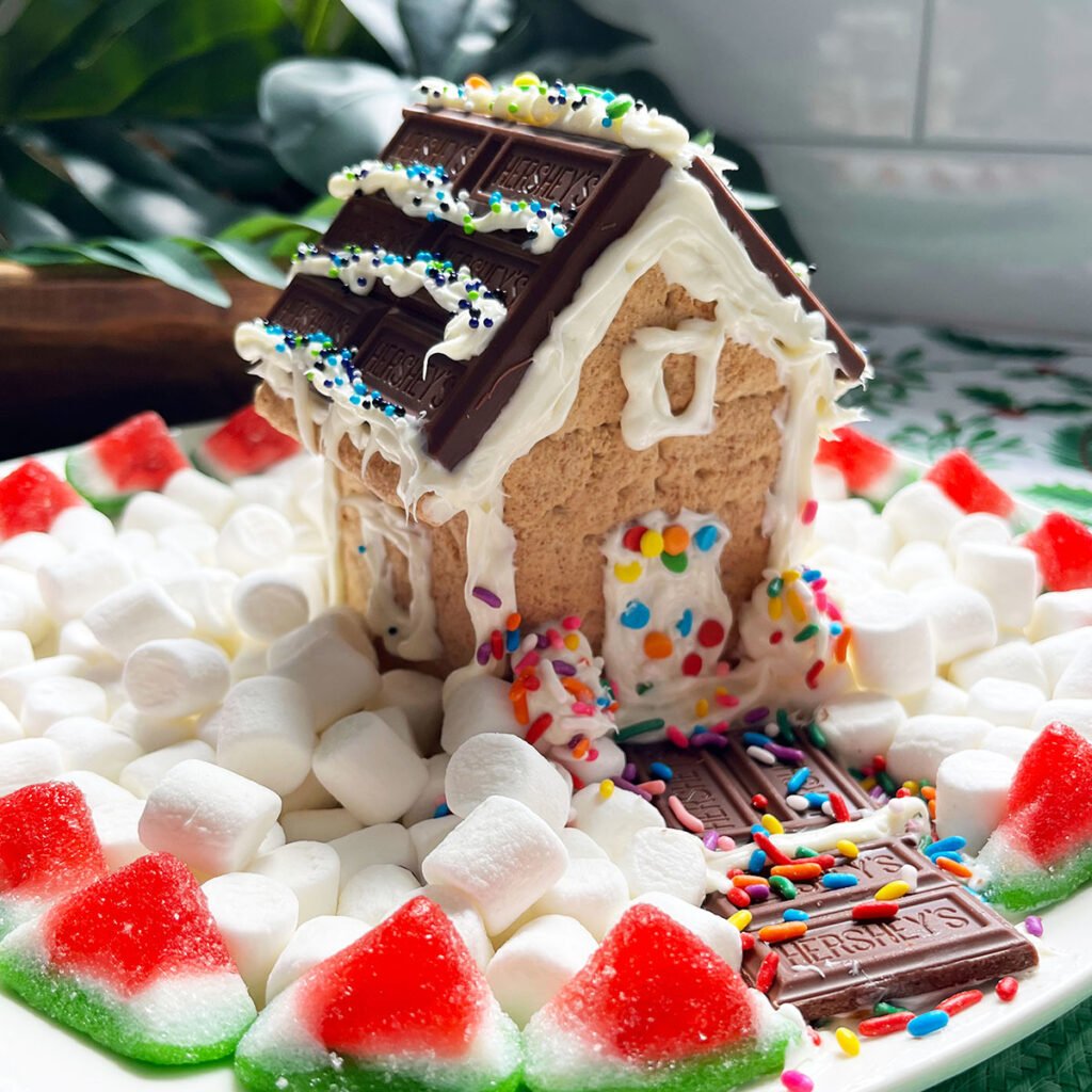 Square feature image of a S'more Gingerbread House made with graham crackers, chocolate bars for a roof and marshmallows for snow.