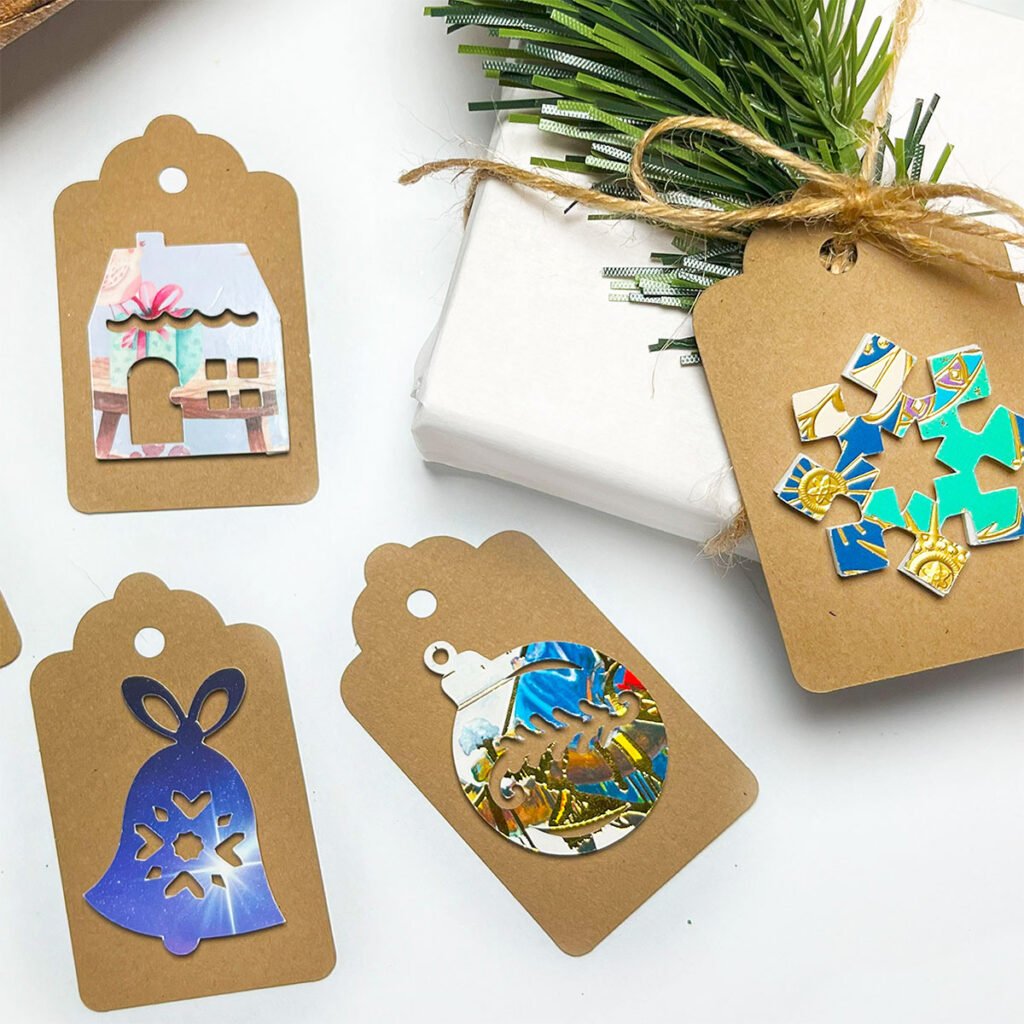 Square feature of recycled Christmas card gift tags. There are four kraft tags with a gingerbread house, a snowflake, a ball ornament and bell.
