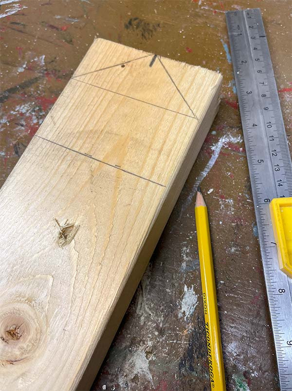 Marking a 2 x 4 by finding the center and marking there. Make a line for the bottom of the roof and angled lines to the center point. Last, measure down three inches from the top and mark a line for the bottom of your house. Now you're ready to cut with a circular saw.