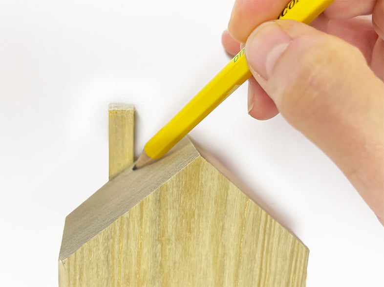 Using the roof line of a wooden house to mark the angle with a pencil to make a chimney. This is an easy way to match the angle of the roof without measuring.