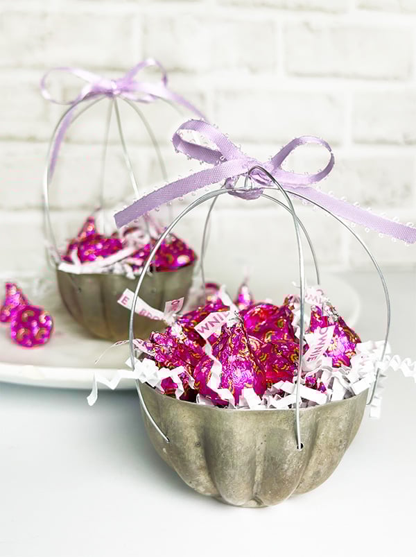Mini baskets made out of vintage round scalloped tart tins and filled with fuchsia Hershey Kisses. To turn these small tart tins into baskets there have been six holes drilled around the edge and wire used to make a sort of bird cage looking basket. Topped with a purple satin ribbon ready for gifting!