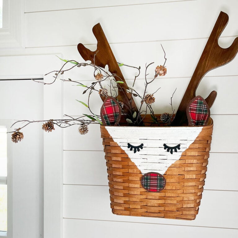 Feature image of a square tapered wicker basket turned into a rustic reindeer basket with the addition of plaid red and green nose and ears and antlers made from an old vintage wall hanging gun rack.