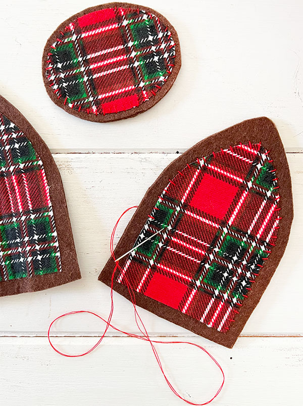 Closeup of red stitching added to the ears and nose to make an upcycled basket. The base of the nose and ears is brown felt with red and green plaid fabric applied with fusible web then hand stitched along the edge for a more finished look.