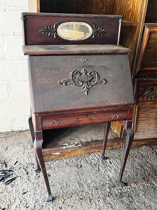 Photo of an old 1923 desk. The desk is completely dusty and untouched in the garage of this old house. It looks like it had never been moved. The finish is mahogany but in great shape with all of the original hardware and trim pieces.