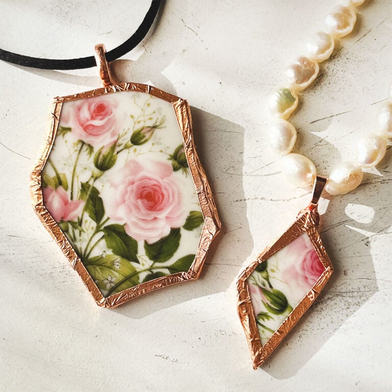 Two pendant made from the same rose pattern broken China Plate. One is larger on a black silk cord and the other is diamond shaped on a string of fresh water pearls.