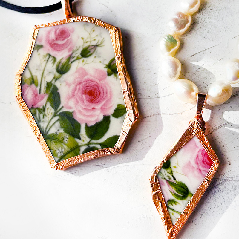 Two pendant made from the same rose pattern broken China Plate. One is larger on a black silk cord and the other is diamond shaped on a string of fresh water pearls.