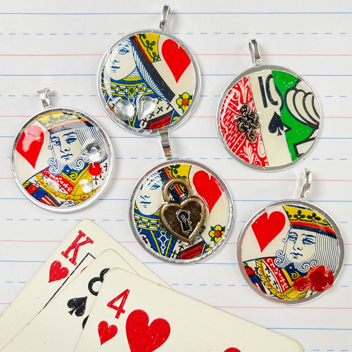 Key tag charms closeup feature of five charms made with king, queen and pieces of vintage playing cards. Overlayed are sparkly read and clear faceted flat back gems and brass tiny mini gems like a heart locket to add dimension. Coated with a thick dome layer of Dimension Mod Podge and a silver jewelry bail matching the silver rim of the key tag glued to the back to make it a necklace pendant.