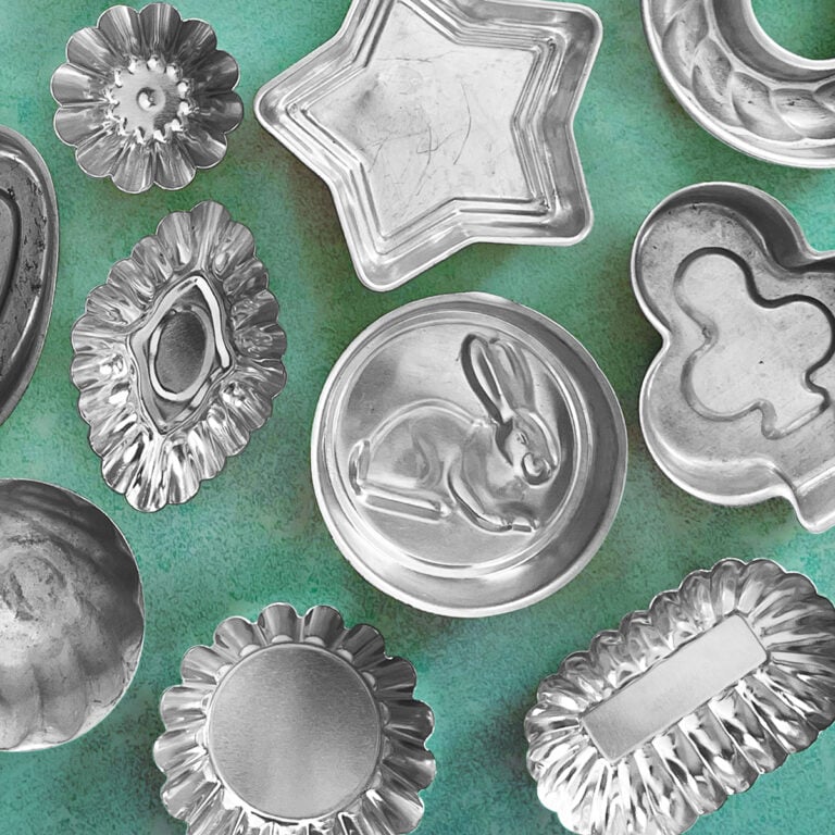 An assortment of different shaped tart tins shown on a vintage aqua background - tins include a bunny tin, a diamond, clover, star, shell and other fluted shapes.