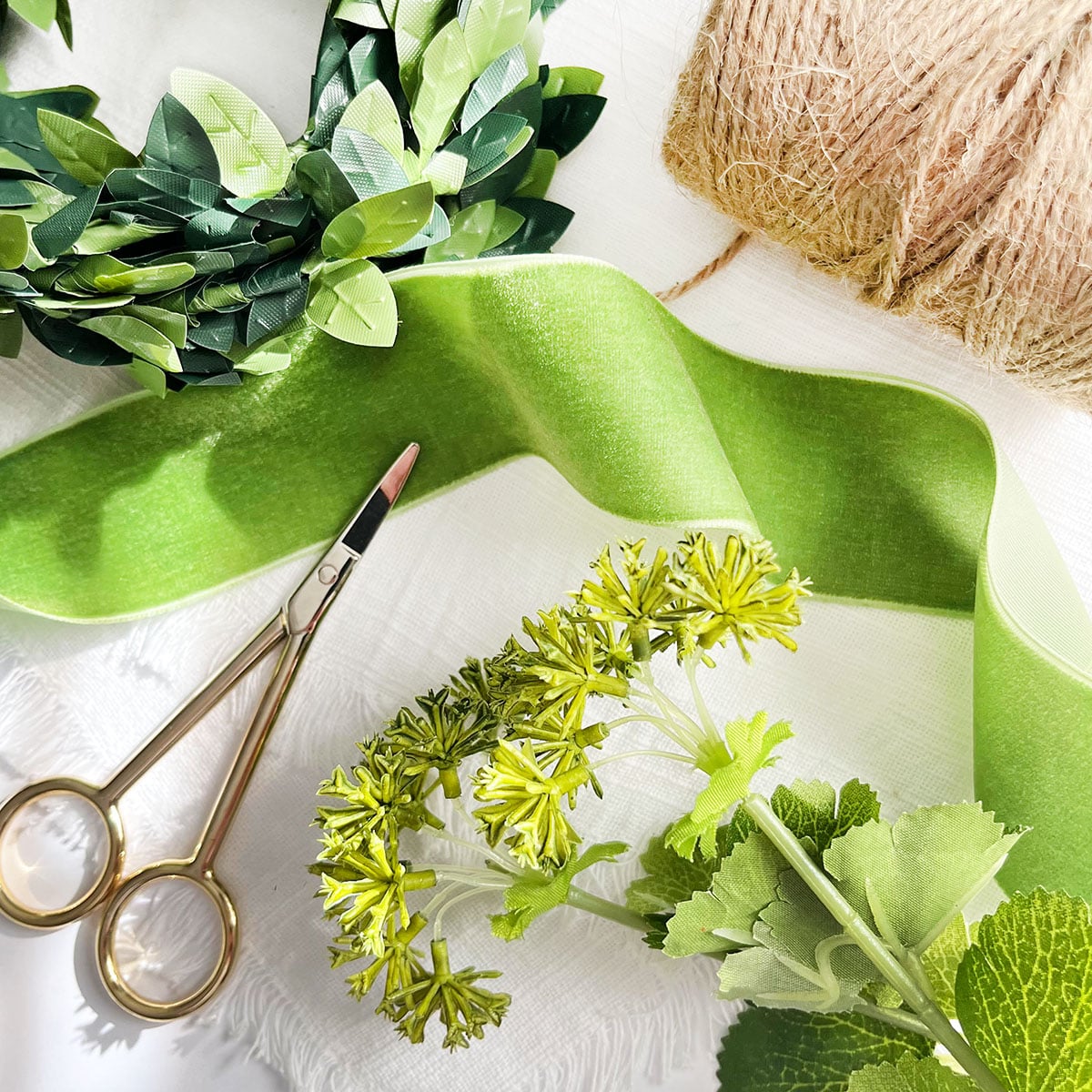 Process of some of the supplies used to make the spring craft ideas roundup post. There is a moss green velvet ribbon, floral green spigs, a small boxwood garland wreath, jute twine and embroidery scissors.