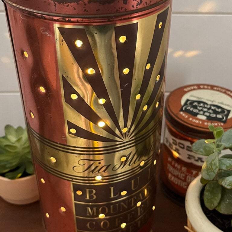 Feature photo for Upcycled Vintage Tins ideas and roundup post. Shown here is a tall tin in copper and chocolate brown - Blue Moutain Coffee. This tin was transformed by using an awl and hammer to poke a hole pattern and add a battery operated candle to the inside to add an array of starlight bursts.