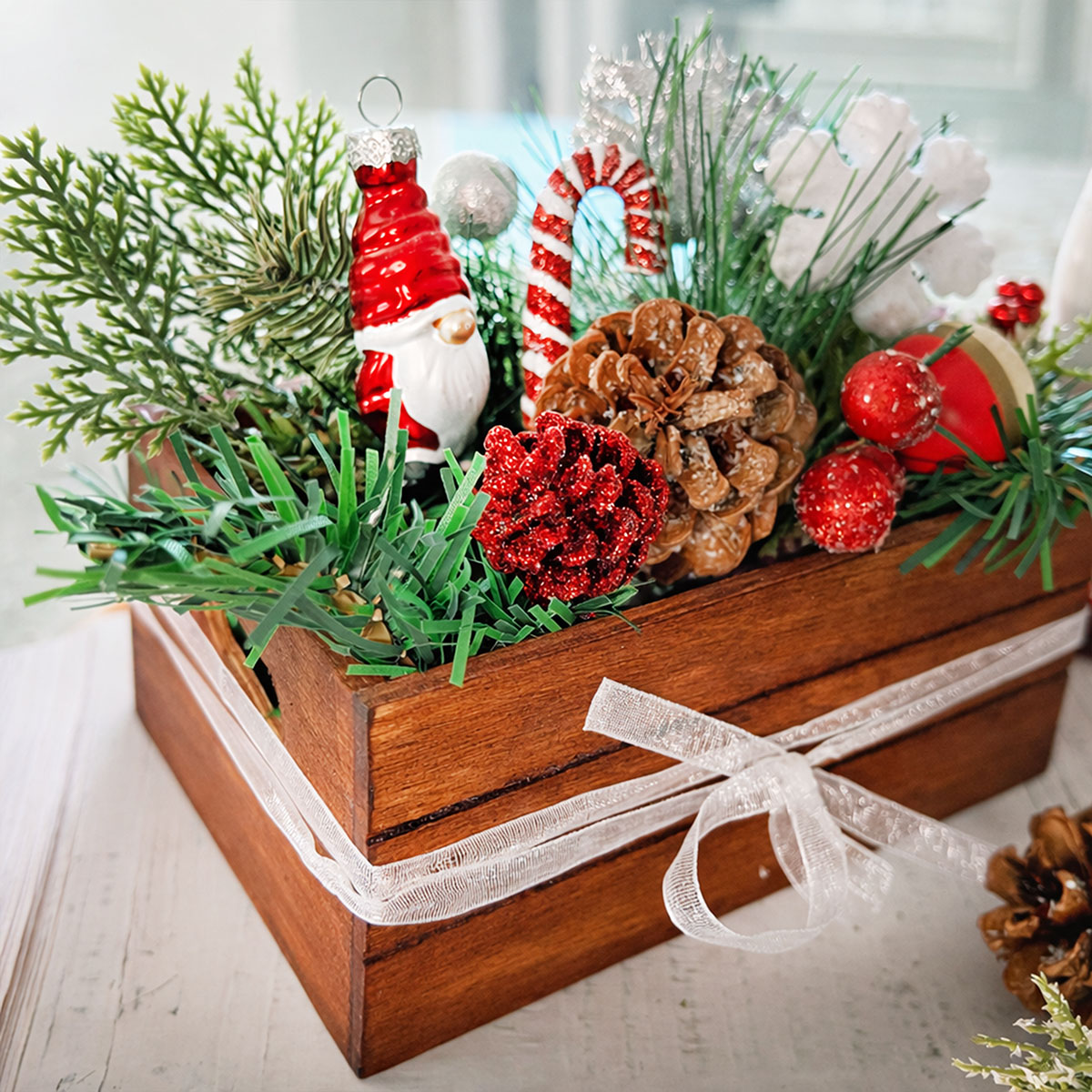 Feature image of a miniature wood crate stained crate shown filled with greenery and miniatures like red berries, pinecones, candy canes and a mini santa gnome ornament.