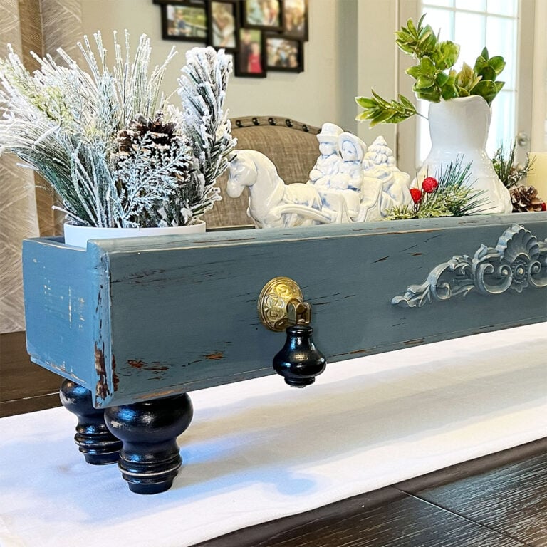 Repurposed drawer turned table riser feature image is a closeup the left side of the drawer, finished with holiday florals and accents inside the drawer set as the centerpiece on a dark wood table.