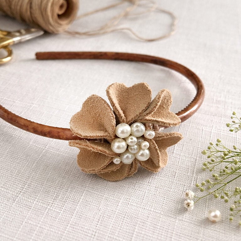 Feature image of a DIY Suede Flower Embellishment on a tortoise shell headband set on a white linen cloth with twine and scissors in the background and soft baby's breath flowers to the side.