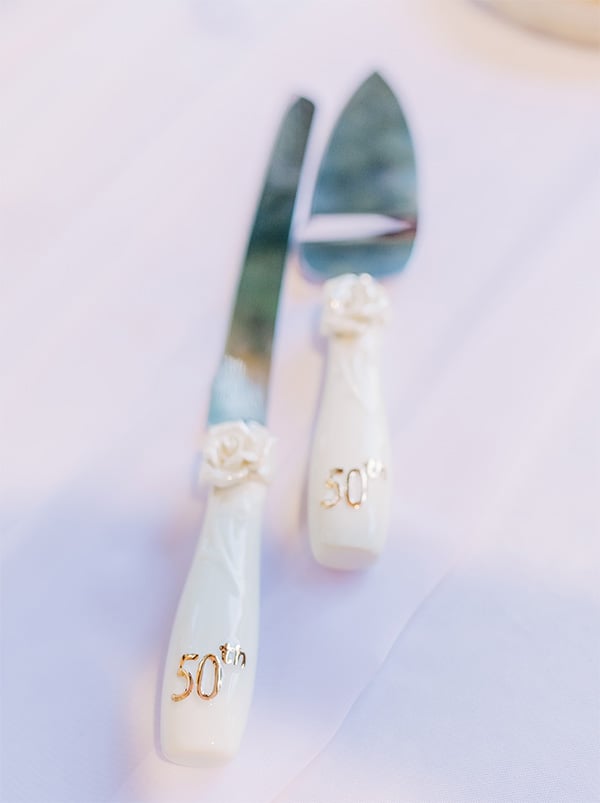 Close up of white handles '50th' in gold on the handles, cake cutting knife and spatula.