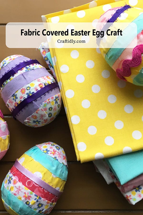 Photo of five finished fabric covered Easter eggs on a table with colorful patterned fabric. These eggs are in pastel fabrics and use satin ribbon and scalloped bric brak ribbon and strips about 1/2 inch of solid and floral patterened fabric.