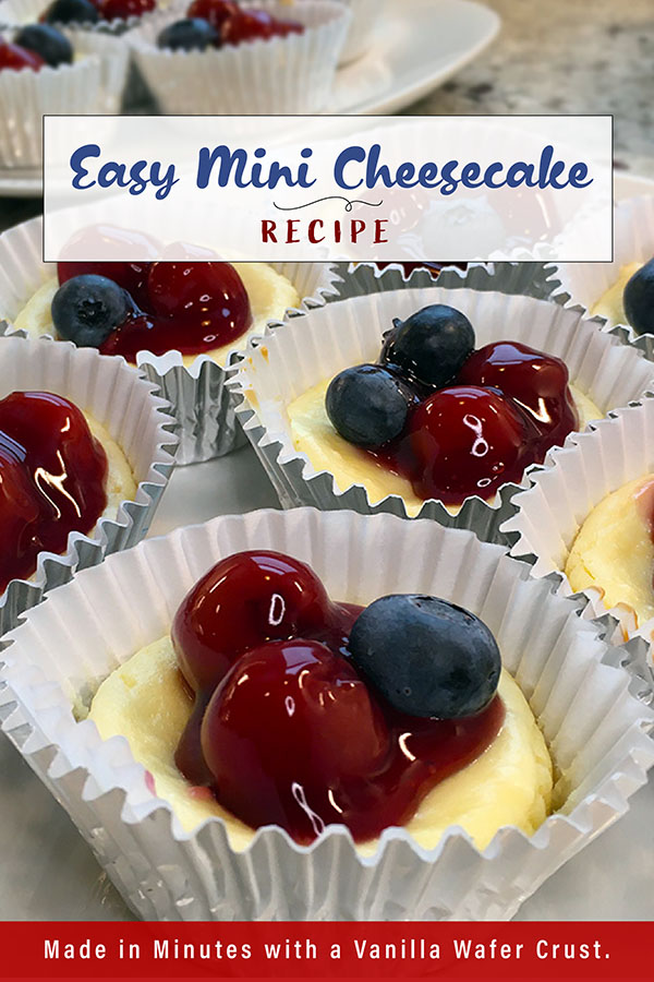 Easy Mini Cheesecakes this is a vertical pinnable image with paper baking cups of individual size cheesecakes topped with cherries in sauce and dotted with blueberries.