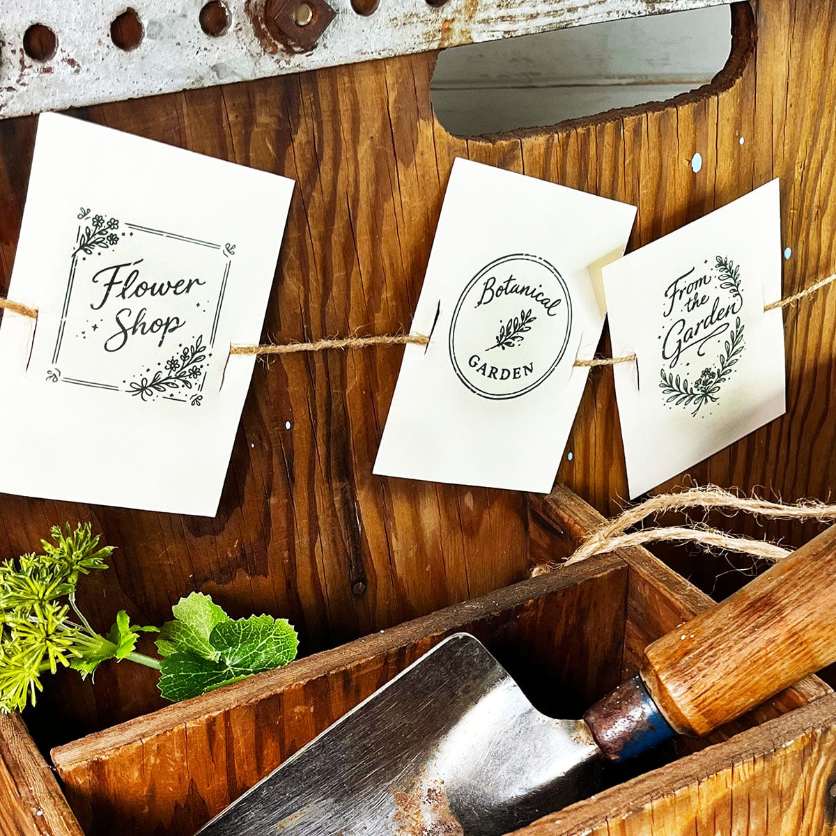 Three botanical cards on ivory paper strung as garland with twine. These are one color line art illustrations in forest green printed on ivory card stock. Flower Shop with a square flower border, Botanical garden, a round seal with a flower in the middle. From the Garden in an oval shpa with leaf motif crest. Simple, beautiful card that can be cut and printed for numerous uses from note cards to ephemera.