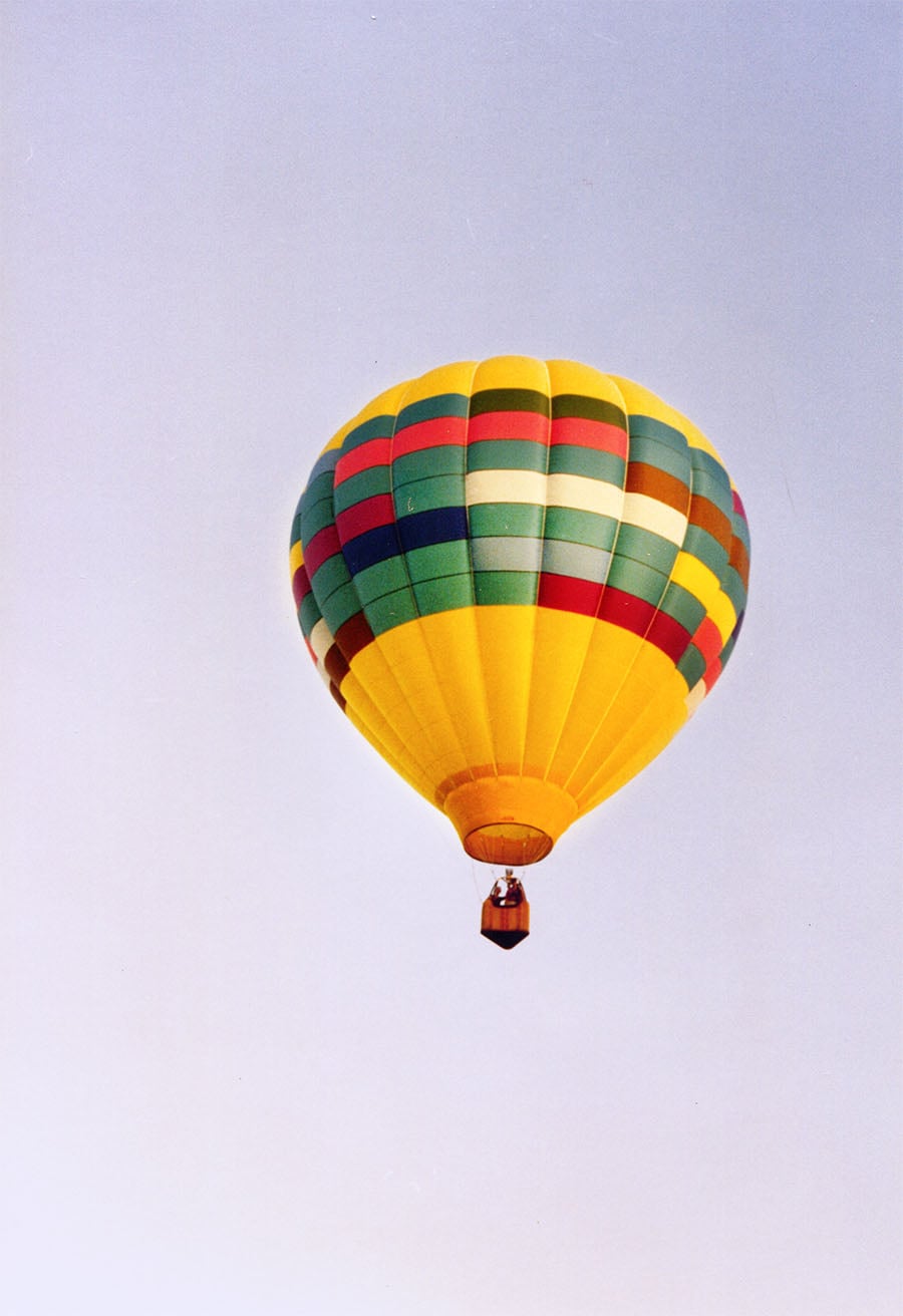 Hot air balloon in the blue clear sky in the colors of yellow as the base and blues and greens.