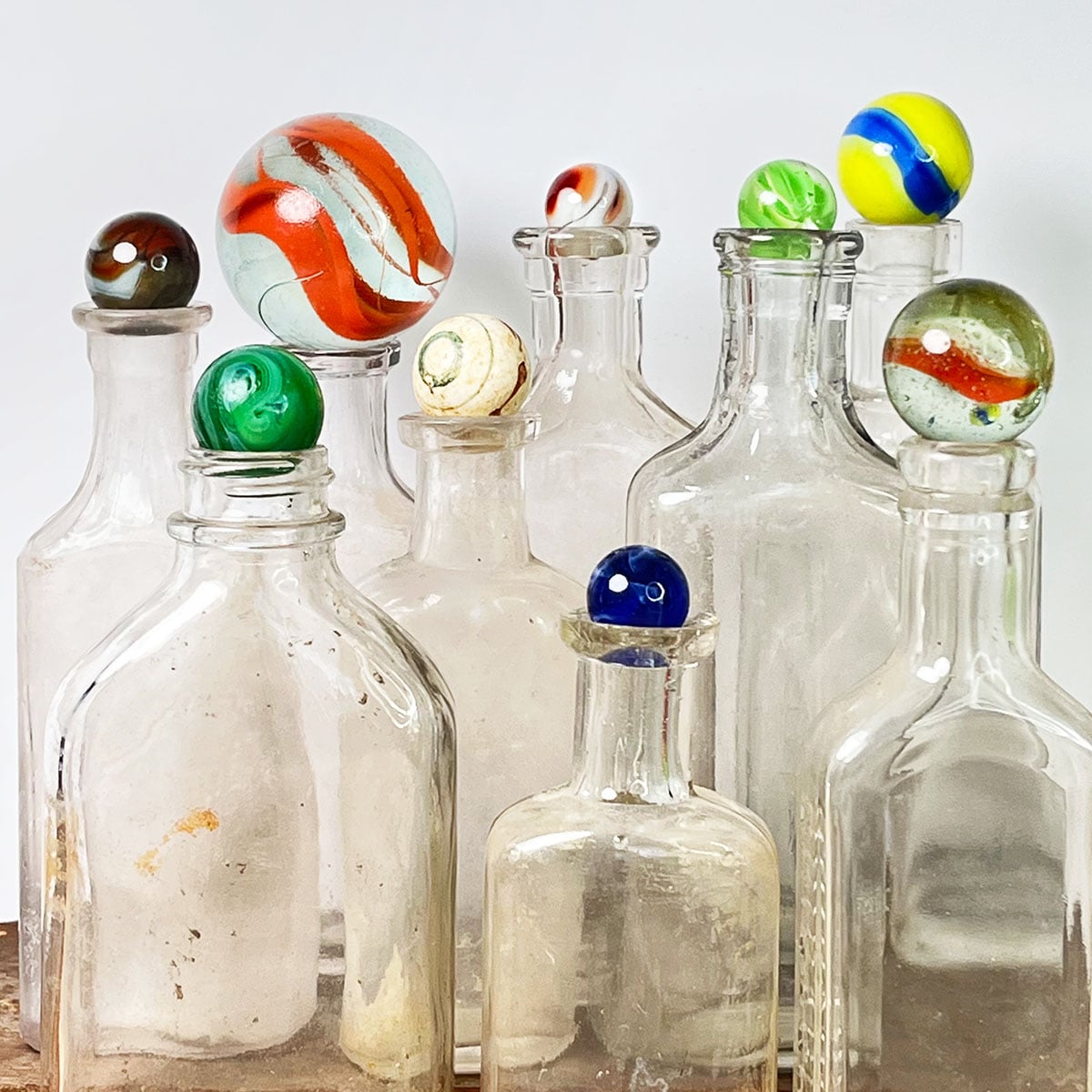 A collection of nine colorful marbles of varying sizes set on top of empty vintage clear bottles.