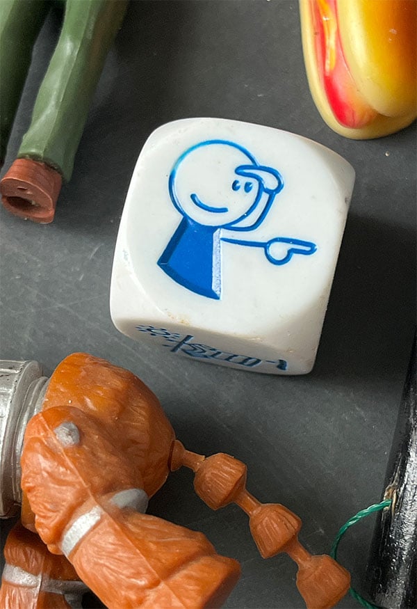 Closeup of a large white dice that has a blue man outline pointing.