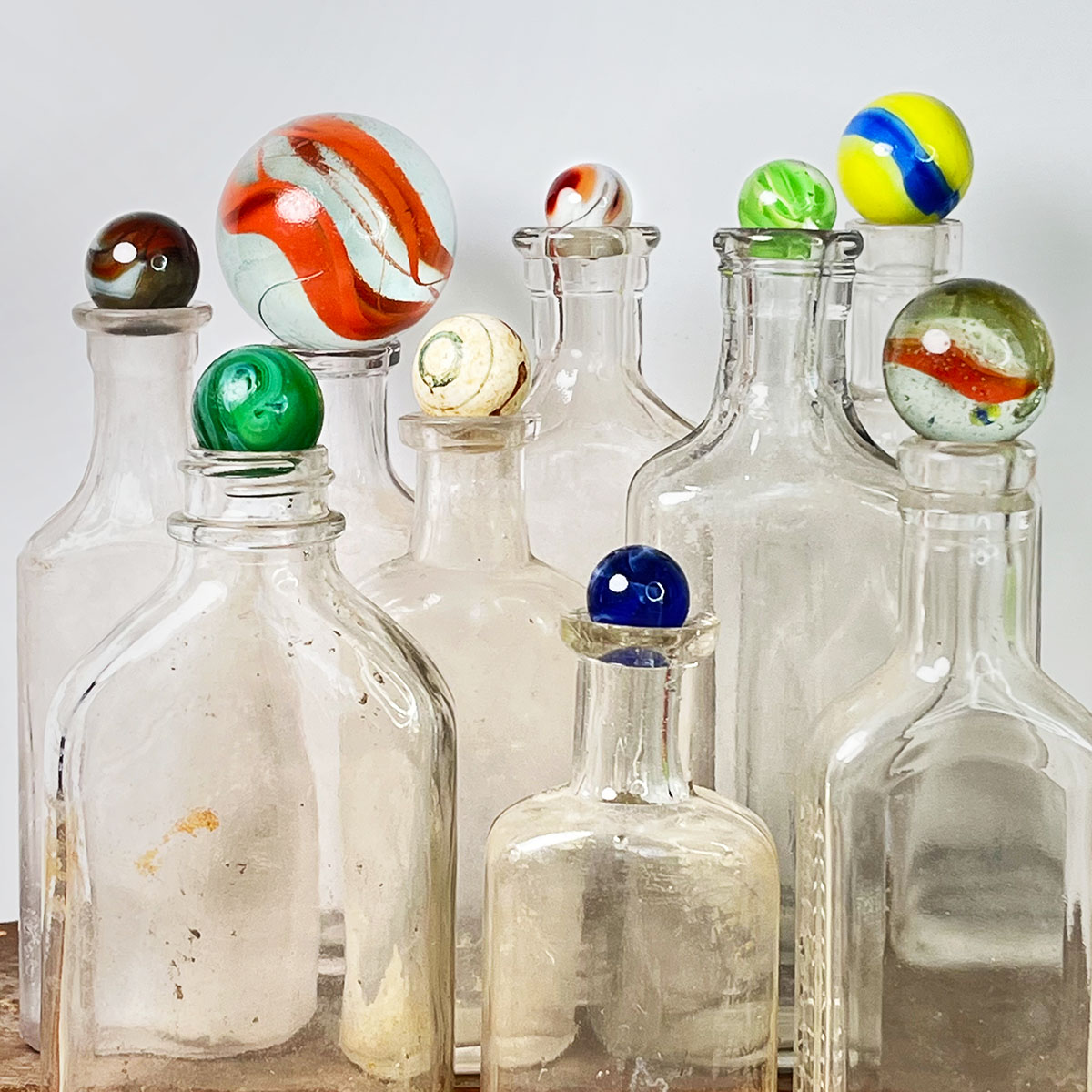 A collection of nine colorful marbles of varying sizes set on top of empty vintage clear bottles.