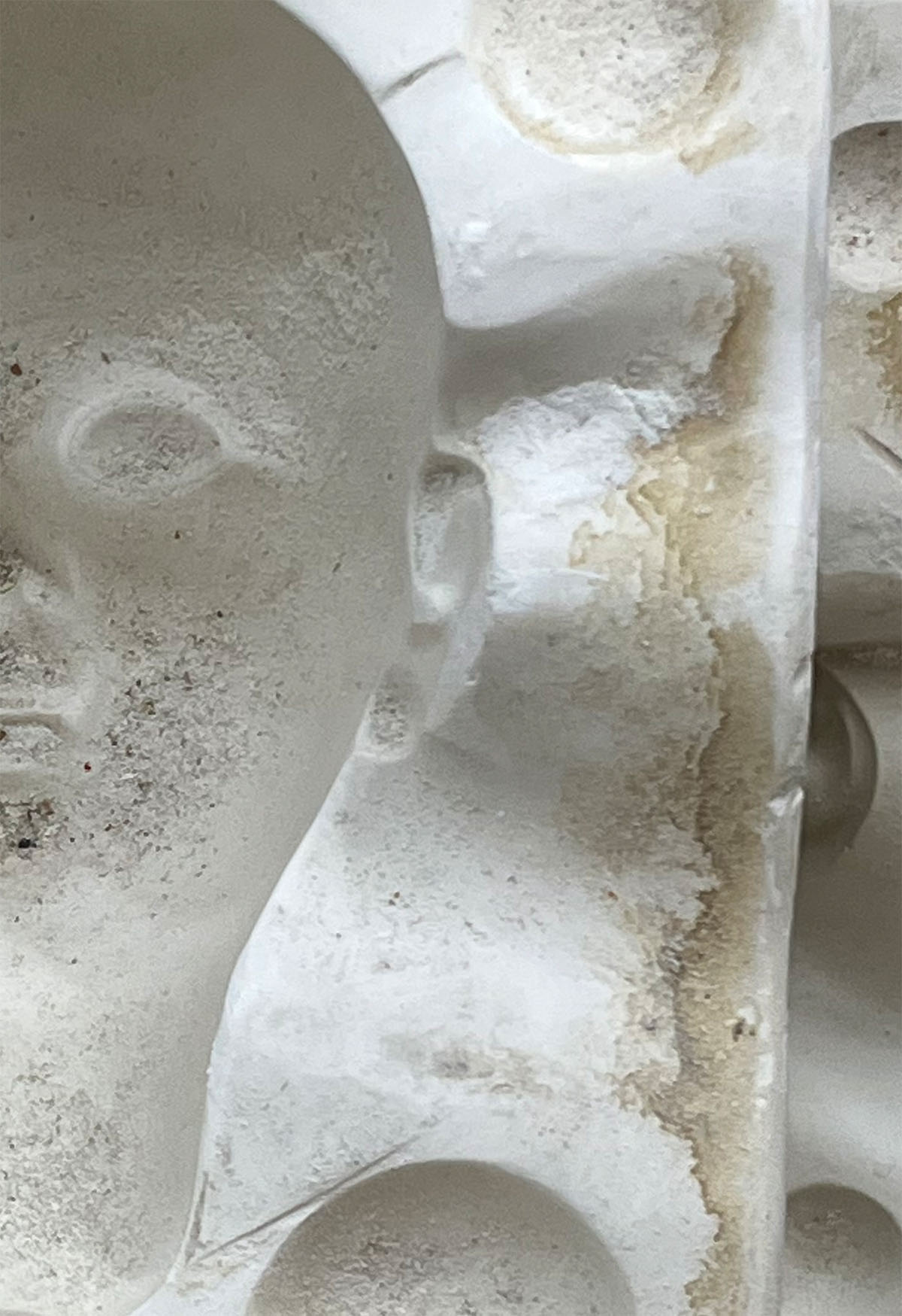 Half of a white ceramic doll mold of a dolls head with shadow areas for the nose, eyes and ears. The white mold has a gritty texture.