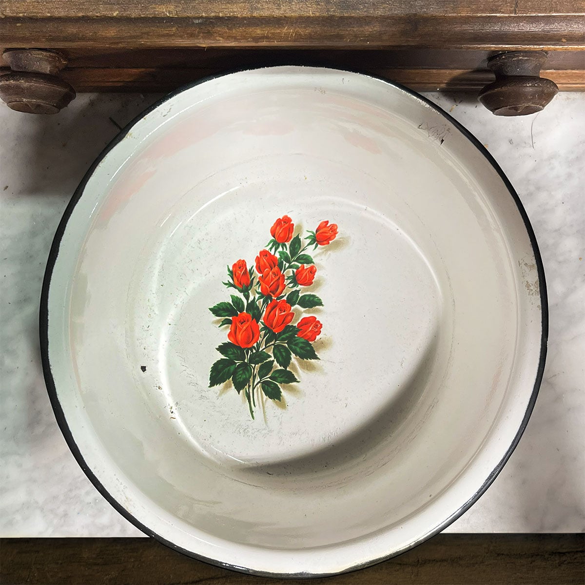 Vintage round white enamelware bowl with a black rim and a bouquet of roses motif printed on the inside repurposed as decor.