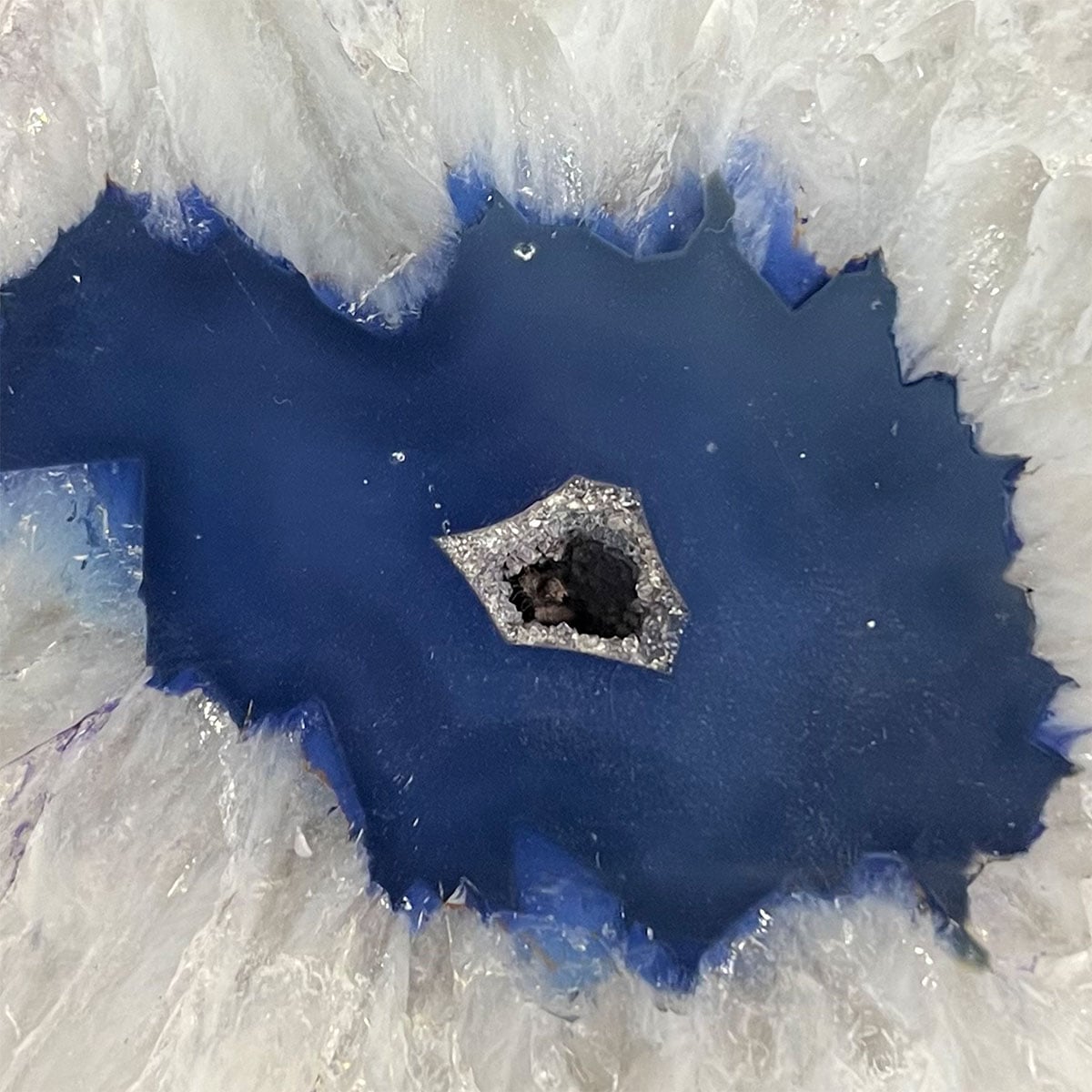 Blue agate geode stone smooth cutawa view with frosty white crystals on the sides and the blue in the center.