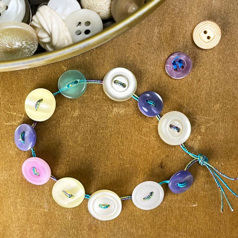 Closeup of a handmade button bracelet made with aqua stretchy cord and buttons in ivory, white, periwinkle, aqua, pipnk and purple.