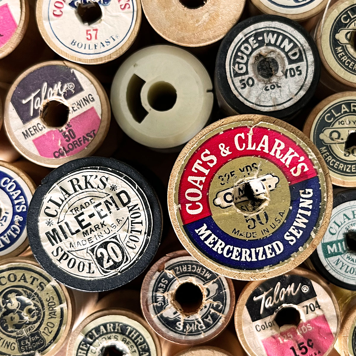 Overhead shot of various vintage wooden and plastic thread spools with advertising from Talon and Coata and Clark's brand.
