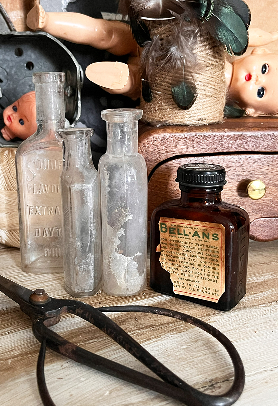 Closeup of ellans vintage brown medicinal bottle, vintage doll faces with piercing eyes, vintage bottles and scissors.
