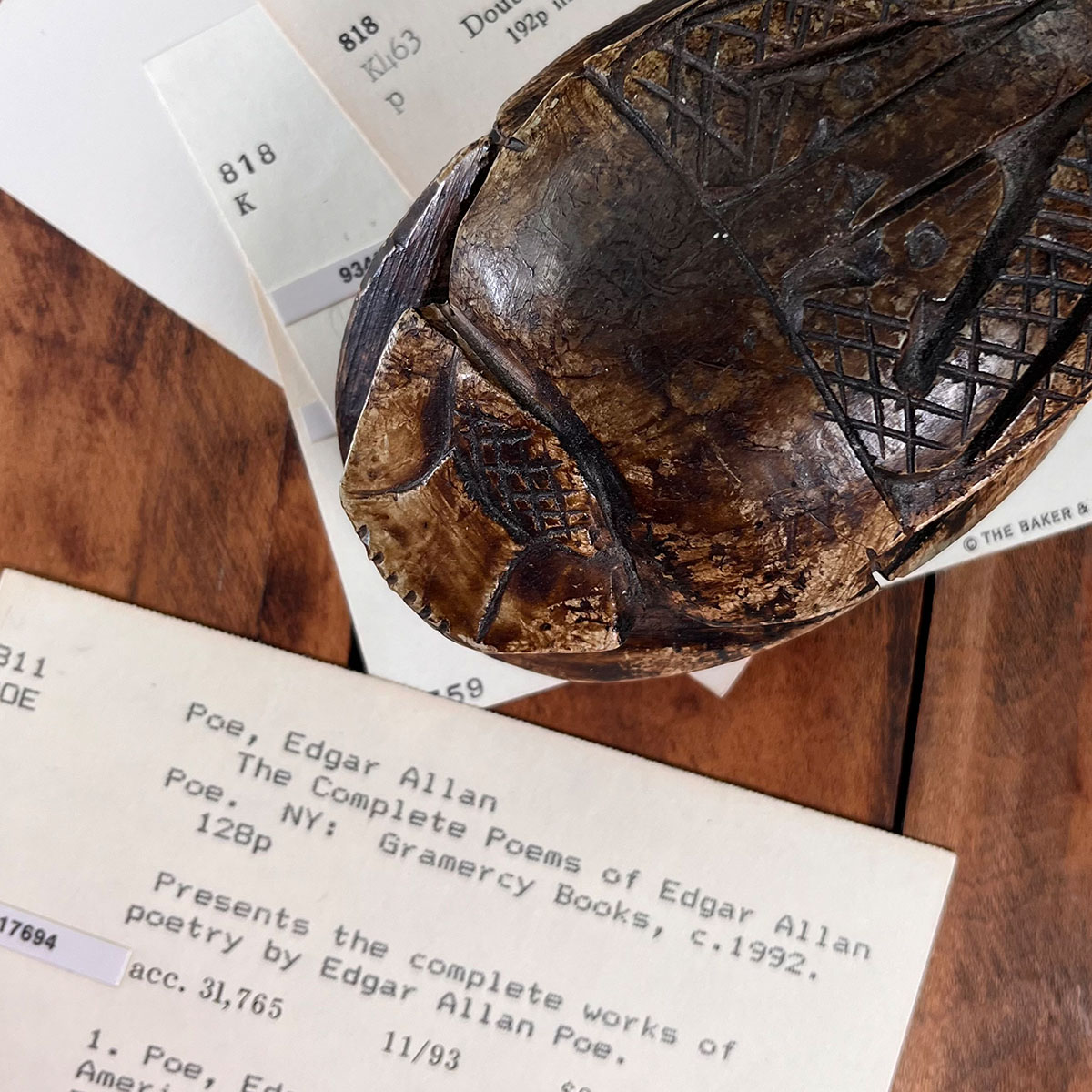 Closeup of a carved stone scarab paperweight and an Edgar Allen Poe, The Complete Poems, vintage manilla card from an old library card catalog.