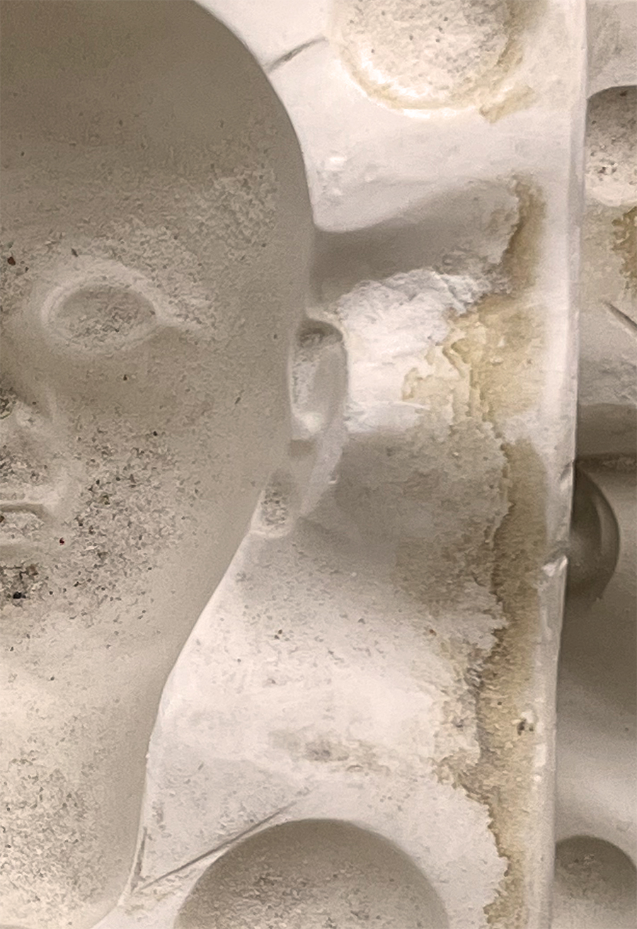 Half of a white ceramic doll mold of a dolls head with shadow areas for the nose, eyes and ears. The white mold has a gritty texture.