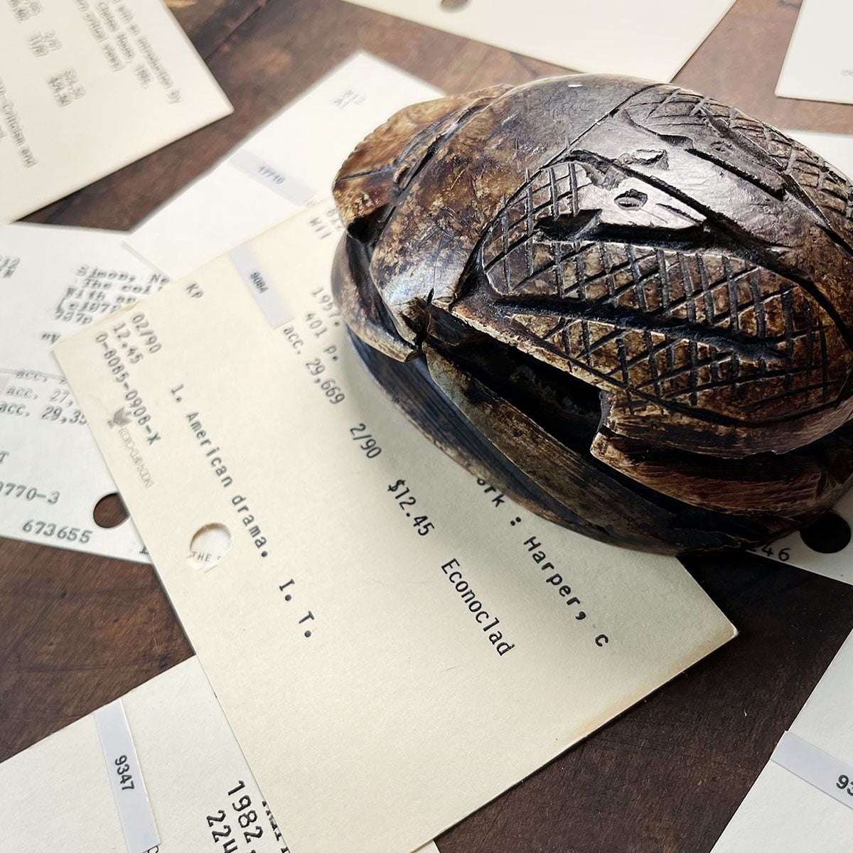 Carved stone scarab paperweight on random cards from an old card catalog.