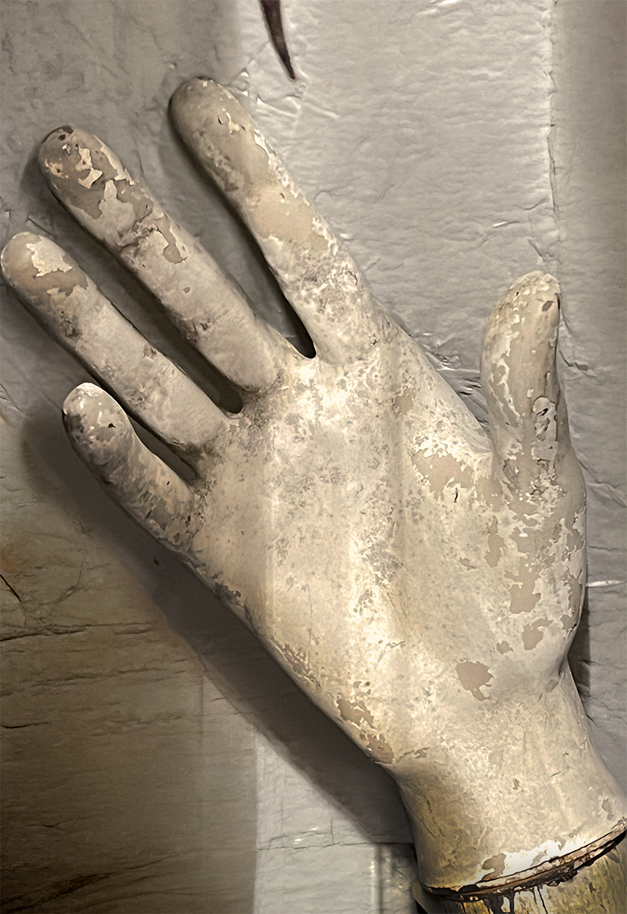Reaching hand from a white mannequin in shadow against a stone wall.
