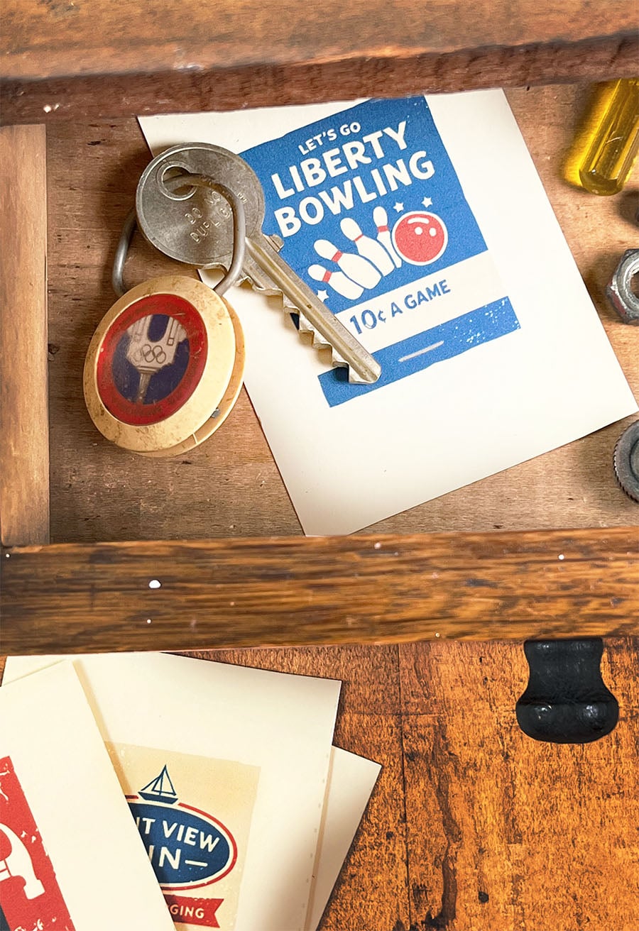 Free pintable vintage-style cards with matchbooks on them. Shown is 'Let's Go Liberty Bowl' in a wood drawer with an old keychain and a few more on the table in front.